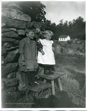 Two young children are standing on chairs in front of a rock wall.
