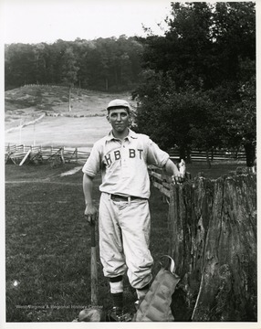 Arnold Metzener, a member of the Helvetia Baseball Team, is standing near a fence and holding a bat.