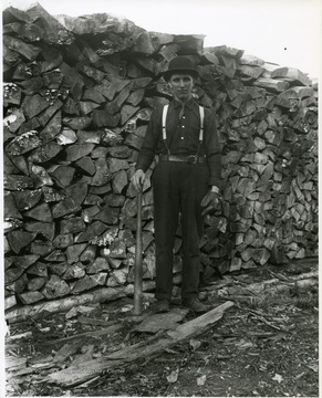 Arnold Metzner with baseball bat and glove standing in front of a large stack of firewood.