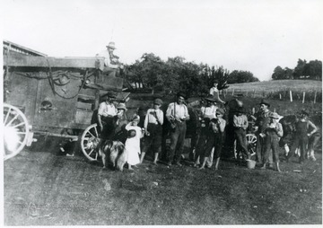 Group of men and children take a break for food and drinks after working with a threshing machine.