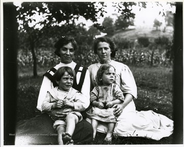 Two women with children on their laps in a field in Helvetia, West Virginia.