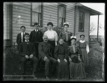A group portrait of a family living in Helvetia, West Virginia. An elderly gentleman and a lady are sitting with three boys and four young ladies in front of a house. 