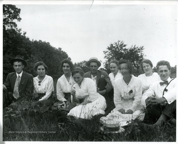 'Group sitting in field; hat on ground in front; Bertha Engler in front with flower.'