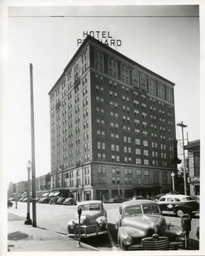 Automobiles are parked in front of the Hotel Prichard building in Huntington, West Virginia. The hotel is located between the Coffee Shoppe and a Drug Store.