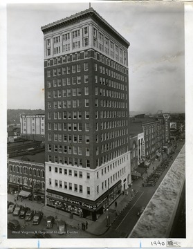 The tall West Virginia Building of Huntington which houses a Walgreen Drug Store on the first floor. Other downtown buildings are also visible, including Hotel Frederick, Angel's Clothing, Gallagher Drugs, United Woolen and Kopy Kat clothing stores.