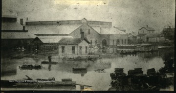 People in boats float around the Ensign Car Works buildings after a flood in 1884.