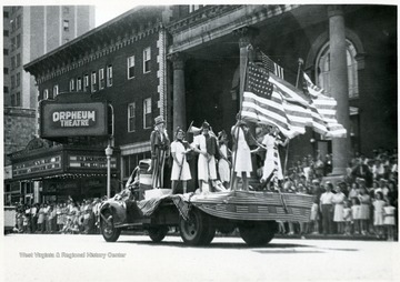 Women with American flags and rifles stand on the bed of a truck in front of the Orpheum Theatre.