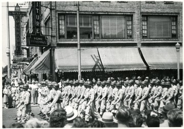 Men in uniform walk down the street in a July 4th military parade.