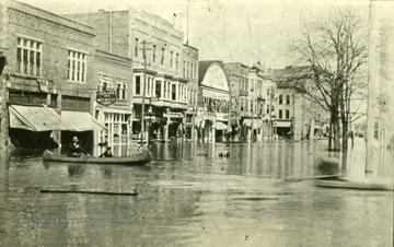 Two men using a canoe to get around town during a flood.  Viewing from the north side of 4th Ave., looking east from 8th street.