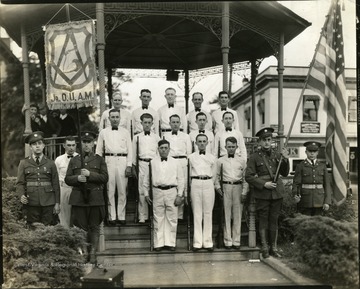 Group portrait of men with guns at their sides.  One man holds a banner, another the American flag.