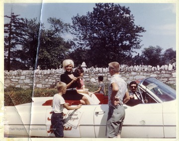 Jayne Mansfield, the Grand Marshall of Martinsburg Centennial Parade and her daughter ride in a car driven by Jim Dailey, sign autographs for two young boys.