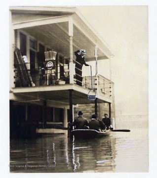 'Charles T. Gorby on porch above Gorby Brothers store fills a grocery order by lowering a bucket which has been added to the photograph. Jesse K. Gorby lived his last years in the apartment to the left of the upper porch; From a photograph in the Wetzel County Historical Museum.'