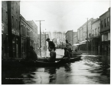 People in canoes float down the street.