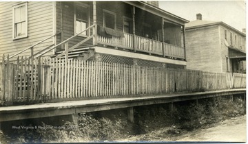 A man is seated on the porch of a house along the sidewalk.
