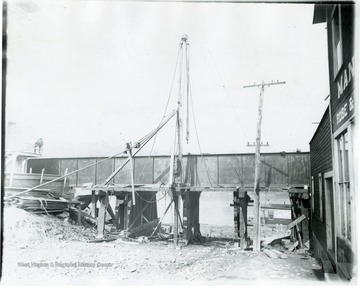 Construction on bridge at foot of Wharf Street. Person sitting near left side of bridge. Electric lines and pole can be seen in front of bridge.