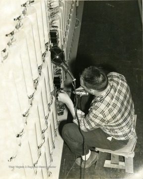 Man installing Centrex using tools, with light hanging above his head. Perhaps the University System? 