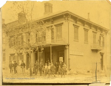 Several men are standing in front of the shop of J.R. Miller, Tobacconist, at the corner of High and Walnut Streets in Morgantown, West Virginia.
