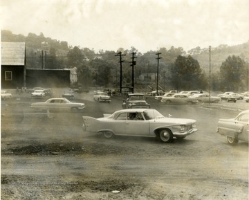 Dust flies as cars exit the Marilla Shirt Factory parking lot.