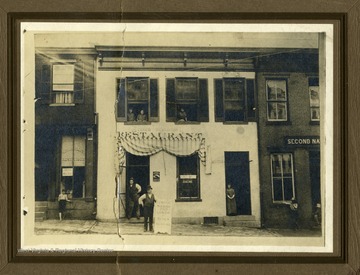 People can be seen in upstairs apartment windows and standing in front of Stines Restaurant, located between Shnatterleys Restaurant and the Second National Bank.