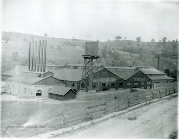 Glass factory in Seneca. Tower seen before the factory, stacks located  on left side of factory. 