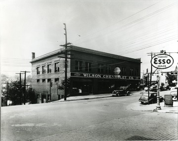 Wilson Chevrolet Company located in Morgantown, W. Va. across from the Standard Esso Dealer. Tow truck located in front of the building. Automobiles line the street. 