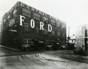 Ford Garage located in Morgantown, W. Va., at the intersection of Chestnut Street and Kirk Street. Large trucks parked near garage. Sign also advertises Mercury.