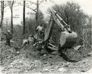 Man using a backhoe to dig in a wooded area while another man watches, Morgantown, W. Va.