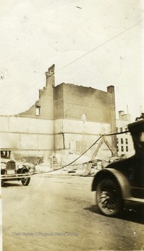 Remains of the Strand Theatre after fire. Cars driving down road in front of structure. 