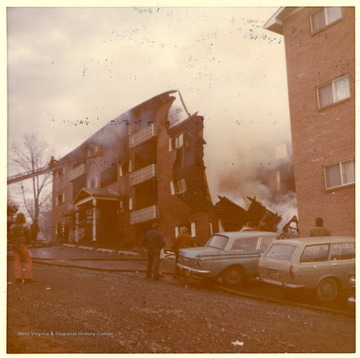 'This picture shows an East Everly Street apartment building which was destroyed by fire on March 20th, 1972. (East Everly Street runs parallel to University Avenue in the vicinity of Pierpont House and the Twin Tower Dorms)  The building was owned by James M. Prete, Morgantown Contractor.  The building contained 15 apartments which housed university students and faculty members.  The fire started at about 12:30 in the afternoon on March 20.  These pictures were shot at about 6:00 in the evening just before the fire was brought under control.  The fire was apparently caused by a spark from the torch of a welder who was working in the attic of the building.  The insulation was ignited and the fire spread down through the walls and across the roof.  The fire provoked a controversy in city council concerning the adequacy of Morgantown's fire fighting equipment.  Mr Prete was also accused of using cheap and unsafe methods in the construction of the building.  These pictures were shot by Miss Carol Wrobleski who lived on Harding Avenue near the site of the fire.'