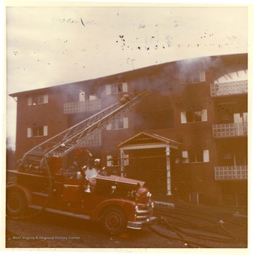 'This picture shows an East Everly Street apartment building which was destroyed by fire on March 20th, 1972. (East Everly Street runs parallel to University Avenue in the vicinity of Pierpont House and the Twin Tower Dorms)  The building was owned by James M. Prete, Morgantown Contractor.  The building contained 15 apartments which housed university students and faculty members.  The fire started at about 12:30 in the afternoon on March 20.  These pictures were shot at about 6:00 in the evening just before the fire was brought under control.  The fire was apparently caused by a spark from the torch of a welder who was working in the attic of the building.  The insulation was ignited and the fire spread down through the walls and across the roof.  The fire provoked a controversy in city council concerning the adequacy of Morgantown's fire fighting equipment.  Mr Prete was also accused of using cheap and unsafe methods in the construction of the building.  These pictures were shot by Miss Carol Wrobleski who lived on Harding Avenue near the site of the fire.'