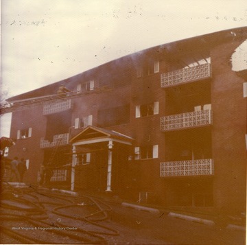 'This picture shows an East Everly Street apartment building which was destroyed by fire on March 20th, 1972. (East Everly Street runs parallel to University Avenue in the vicinity of Pierpont House and the Twin Tower Dorms) The building was owned by James M. Prete, Morgantown Contractor. The building contained 15 apartments which housed University students and faculty members. The fire started at about 12:30 in the afternoon on March 20. These pictures were shot at about 6:00 in the evening just before the fire was brought under control. The fire was apparently caused by a spark from the torch of a welder who was working in the attic of the building. The insulation was ignited and the fire spread down through the walls and across the roof. The fire provoked a controversy in city council concerning the adequacy of Morgantown's fire fighting equpiment. Mr. Prete was also acused of using cheap and unsafe methods in the construction of the building. These pictures were shot by Miss Carol Wrobleski who lived on Harding Avenue near the site of the fire.'