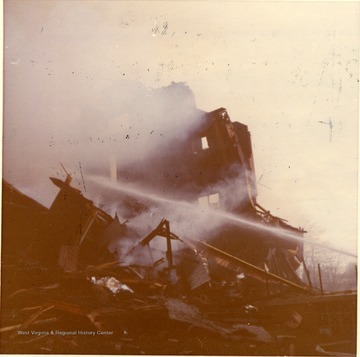 'This picture shows an East Everly Street apartment building which was destroyed by fire on March 20th, 1972. (East Everly Street runs parallel to University Avenue in the vicinity of Pierpont House and the Twin Tower Dorms) The building was owned by James M. Prete, Morgantown Contractor. The building contained 15 apartments which housed University students and faculty members. The fire started at about 12:30 in the afternoon on March 20. These pictures were shot at about 6:00 in the evening just before the fire was brought under control. The fire was apparently caused by a spark from the torch of a welder who was working in the attic of the building. The insulation was ignited and the fire spread down through the walls and across the roof. The fire provoked a controversy in city council concerning the adequacy of Morgantown's fire fighting equpiment. Mr. Prete was also acused of using cheap and unsafe methods in the construction of the building. These pictures were shot by Miss Carol Wrobleski who lived on Harding Avenue near the site of the fire.'