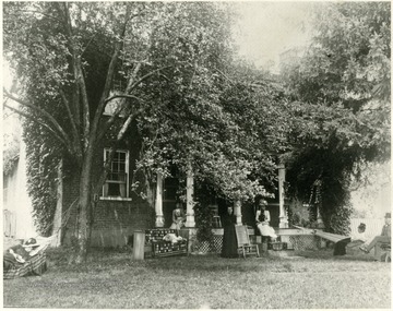 'Now the WVU State Agricultural Farm.' Ladies sit on the porch of a brick home obscured by trees.