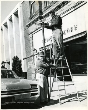 Two men attach the High St. sign and the Bank St. signs on High St.