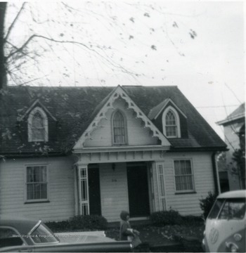 Front view of the Cox house on Kingwood Street in Morgantown, W. Va. A child walks by the house behind the automobiles parked in front of the house. 