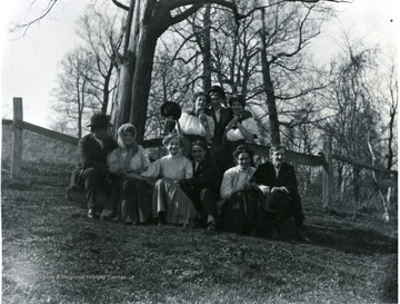 A group of people pose outdoors for a photo. One guy, in the middle, making a funny face. Picture taken near a fence. 