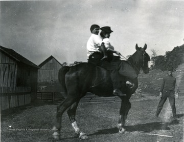A young woman and young man seen riding a horse. Another man stands on ground in front of horse. 