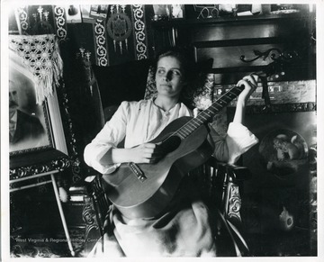 A woman is sitting in a rocking chair playing guitar in a house in Morgantown, West Virginia.