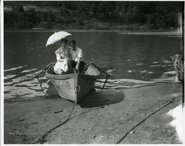 Woman is holding an umbrella as the boat straddles the shore.