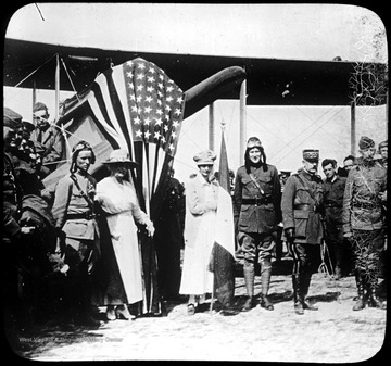 World War I Lantern Slide Show. Slide No. 54 in group of originally numbered slides.  Group portrait in front of biplane draped with American flag.  Includes pilots, soldiers, and two female civilians.  Frame is labelled with text saying 'Visual Bureau, University of Pittsburgh.'  (negative no. 54-12450 is inscribed on slide)<br /><br /><br />