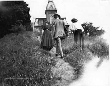 A man and two women are walking on a path towards Woodburn on the campus of West Virginia University.