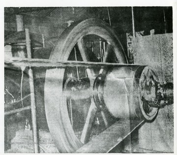 "This huge gas engine is the source of power for the pumping of at least 25 oil wells in the Volcano area. Oil, once plentiful in the vicinity, has been used up to such an extent that production costs must be kept to a minimum by the use of cheap power. The engine power is transferred to the pumps by means of an endless cable.'--Back of photograph. 'William C. Stiles, Jr. introduced the endless cable  pumping system in 1874. He did not invent the endless cable system but was the first to use it in the production of oil. The John Roebling Comapny (NY) manufactured the cable used. This same cable used when Roebling built the Brooklyn Bridge. Roebling's son, Washington Roebling, played a very keen role in the Union victory of Gettysburg. Roebling never bothered to protect their cable-consided it to be a bother. The large wheel in this photo is a band wheel. It transfers the power from the engine to the endless cable system. The belt shown is probably leather. The power is geared up by passing over three belted wheels. The last wheel have a diameter of 18 feet. The 18 foot wheel travel very slowly, but very powerfully. Form it the power transfered to the cable system.'--Mike Naylor, 03/2006.