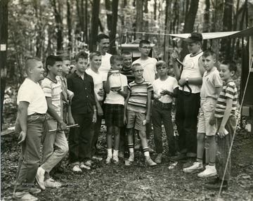 Boys and men gather for a picture. Some of the boys can be seen holding snakes, either directly holding on to the snake or in a container. Two of the members are 'John Neal and Tom Howard'. 