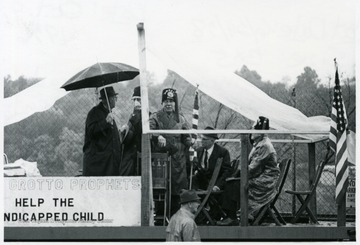 Group of men sit on a raised platform with a banner that reads 'Grotto Prophets Help the Handicapped Child.'