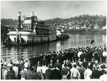 A crowd, including a marching band, gathered on the shore of the Monongahela River to watch the arrival of the Showboat Rhododendron.