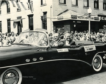 Justice Bowers and Harley O. Staggers ride in a convertible in a Labor Day parade on High Street at the corner of High and Pleasant Streets. 