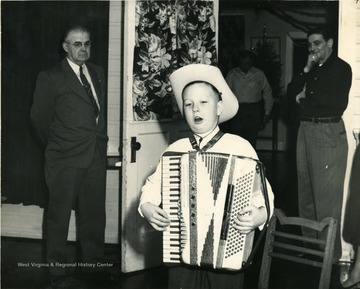 Child wearing a cowboy hat, singing, and playing an accordion. 'Labor Temple.'