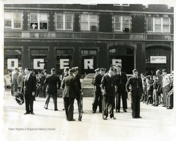 Men in uniform celebrating Veterans Day in front of the Monongalia County Courthouse in Morgantown, West Virginia. Roger's Florist Store is in the background.