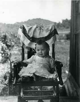 A baby sits in a rocking chair for a picture. 