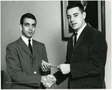 'Louis Barker of Dunbar, Kanawha County, left, senior in the School of Pharmacy at West Virginia University, is shown being presented the Kappa Psi scholastic achievement award by Chester Friedl, president of the local chapter.  The award is $25 in textbooks presented by the local chapter, Beta Eta, to the student who makes the highest grades during his junior year.  Barker is the son of Mr. and Mrs. Lawrence Barker.  Friedl is the son of Mr. and Mrs. Joseph Friedl, Athens, Mercer County.'